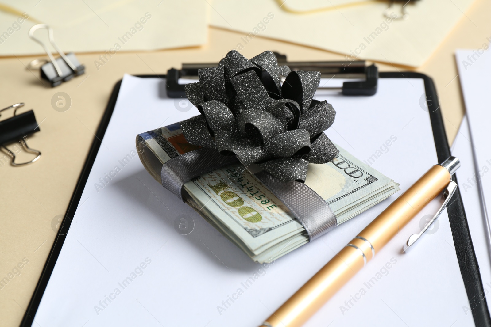 Money bonus. Dollar banknotes with bow, pen, clipboard and binder clips on beige background, closeup Photo of Money bonus. Dollar banknotes with bow, pen, clipboard and binder clips on beige background, closeup