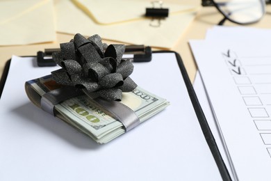Photo of Money bonus. Dollar banknotes with bow, clipboard and checklist on table, closeup