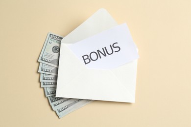 Photo of Card with word Bonus, envelope and dollar banknotes on beige background, flat lay