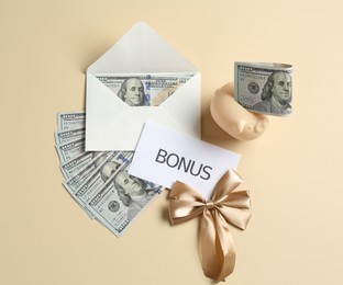 Photo of Card with word Bonus, envelope, dollar banknotes, bow and piggy bank on beige background, flat lay