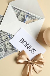 Photo of Card with word Bonus, envelope, dollar banknotes and bow on beige background, flat lay