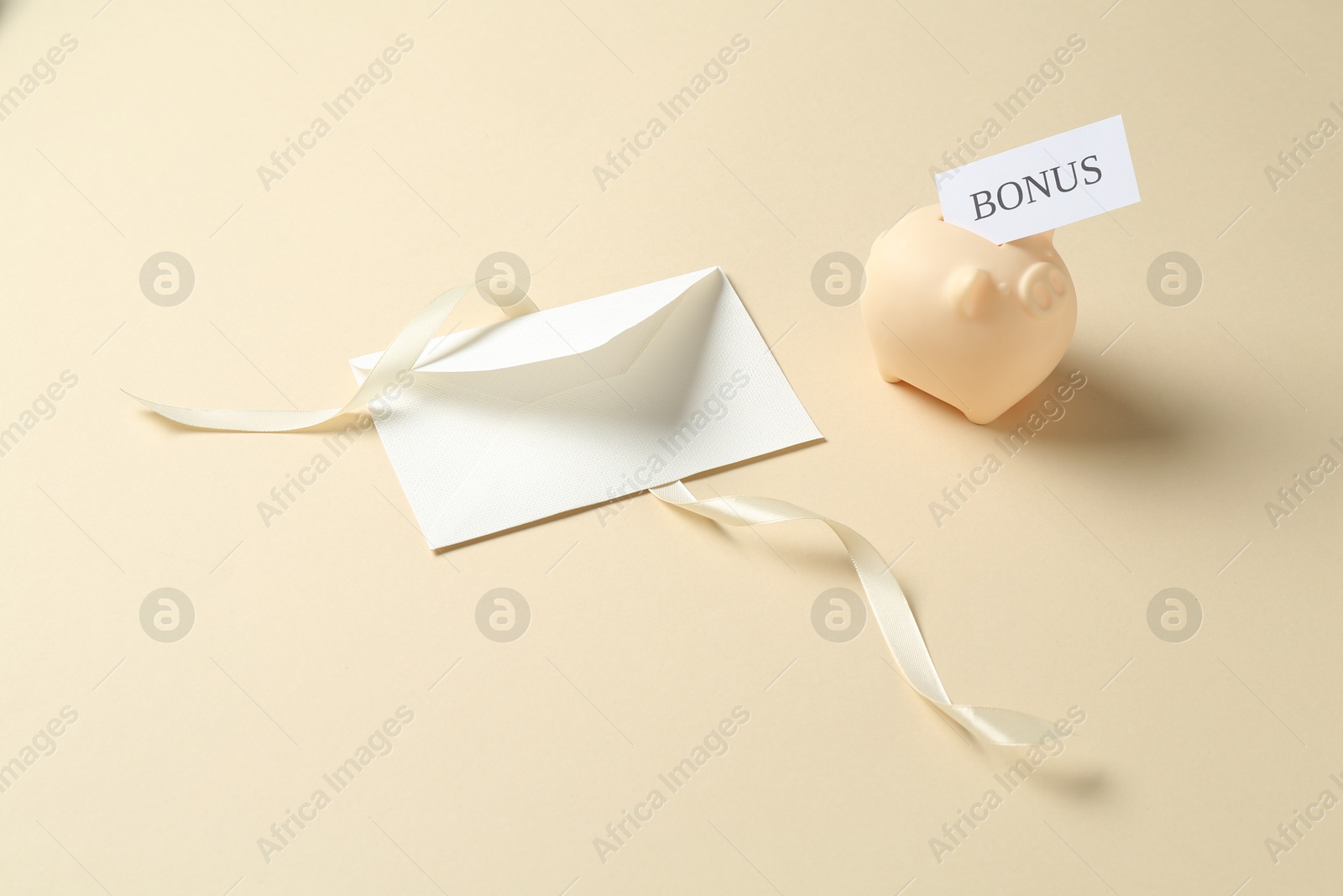 Card with word Bonus, envelope, ribbon and piggy bank on beige background Photo of Card with word Bonus, envelope, ribbon and piggy bank on beige background