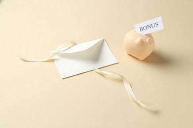 Photo of Card with word Bonus, envelope, ribbon and piggy bank on beige background