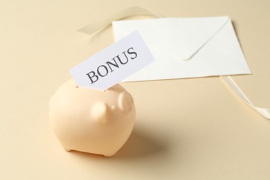 Photo of Card with word Bonus, piggy bank, envelope and ribbon on beige background, closeup