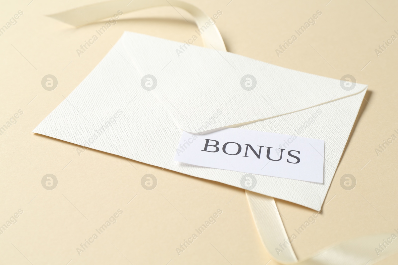 Card with word Bonus, envelope and ribbon on beige background, closeup Photo of Card with word Bonus, envelope and ribbon on beige background, closeup