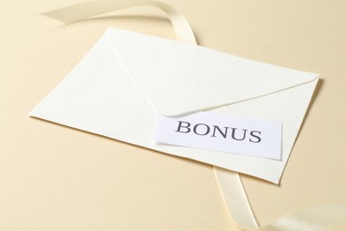 Photo of Card with word Bonus, envelope and ribbon on beige background, closeup