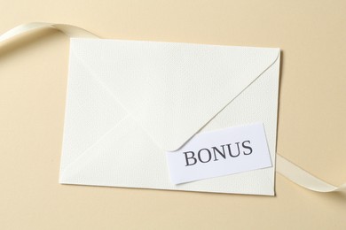 Photo of Card with word Bonus, envelope and ribbon on beige background, top view