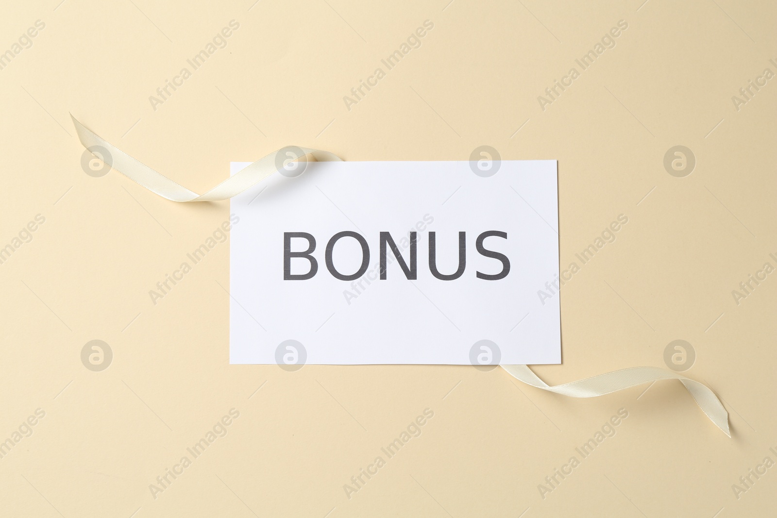Card with word Bonus and ribbon on beige background, top view Photo of Card with word Bonus and ribbon on beige background, top view