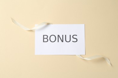 Photo of Card with word Bonus and ribbon on beige background, top view