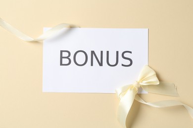 Photo of Card with word Bonus and bow on beige background, flat lay