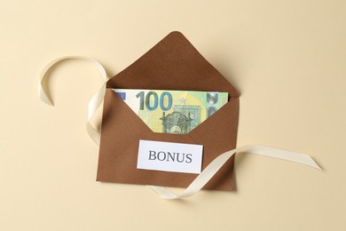 Photo of Money bonus. Envelope with euro banknote and ribbon on beige background, top view