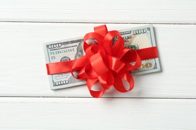 Photo of Money bonus. Dollar banknotes with bow on white wooden table, top view