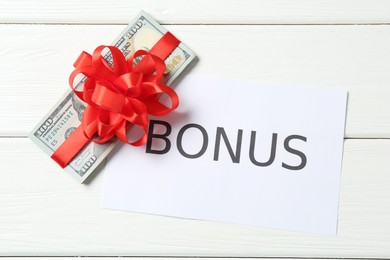 Photo of Money bonus. Dollar banknotes with bow and card on white wooden table, flat lay