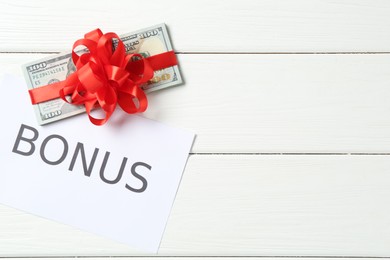 Photo of Money bonus. Dollar banknotes with bow and card on white wooden table, flat lay. Space for text