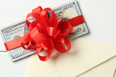 Photo of Money bonus. Dollar banknotes with bow and envelope on white wooden table, flat lay
