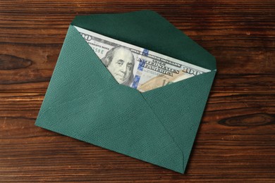 Photo of Money bonus. Envelope with dollar banknote on wooden table, top view