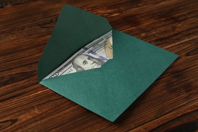 Photo of Money bonus. Envelope with dollar banknote on wooden table, closeup