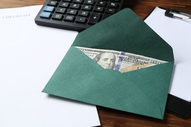 Photo of Money bonus. Envelope with dollar banknote, clipboard, checklist and calculator on wooden table, closeup