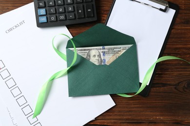Photo of Money bonus. Envelope with dollar banknote, clipboard, checklist, ribbon and calculator on wooden table, flat lay