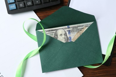 Photo of Money bonus. Envelope with dollar banknote, clipboard, ribbon and calculator on wooden table, flat lay