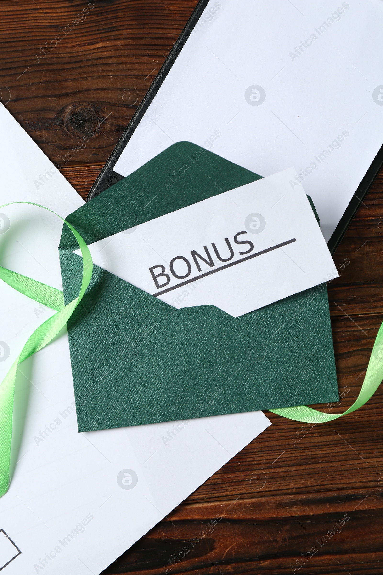 Card with word Bonus, envelope, ribbon and clipboard on wooden table, flat lay Photo of Card with word Bonus, envelope, ribbon and clipboard on wooden table, flat lay
