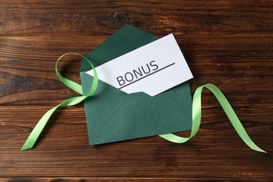 Photo of Card with word Bonus, envelope and ribbon on wooden table, top view