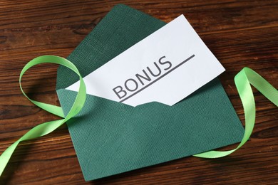 Photo of Card with word Bonus, envelope and ribbon on wooden table, above view
