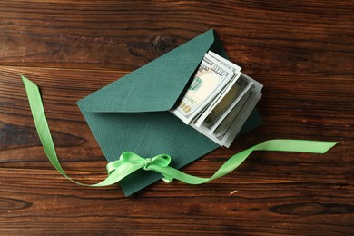 Photo of Money bonus. Envelope with dollar banknotes and ribbon on wooden table, top view