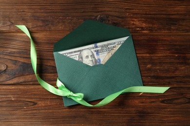 Photo of Money bonus. Envelope with dollar banknote and ribbon on wooden table, top view