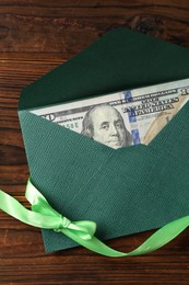 Photo of Money bonus. Envelope with dollar banknote and ribbon on wooden table, top view
