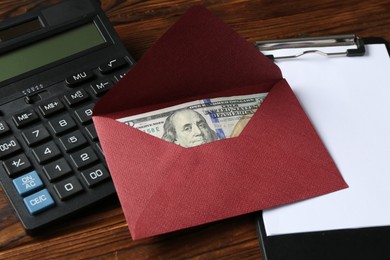 Photo of Money bonus. Envelope with dollar banknote, clipboard and calculator on wooden table