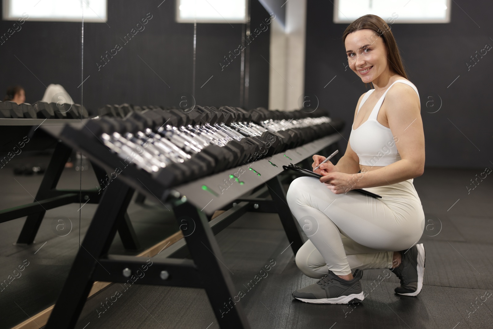 Photo of Personal trainer with clipboard and dumbbells in sport center