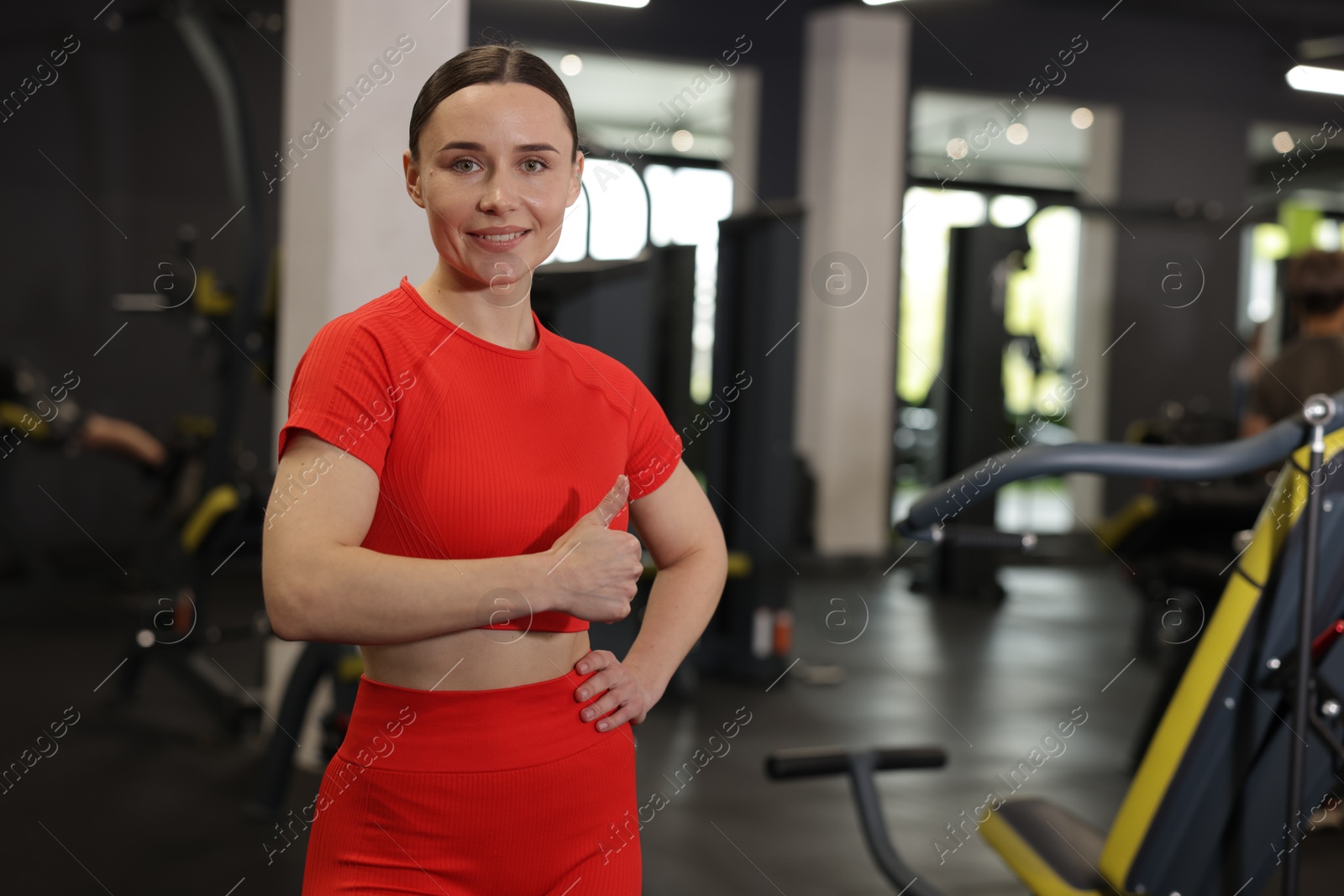Photo of Personal trainer showing thumbs up in gym. Space for text