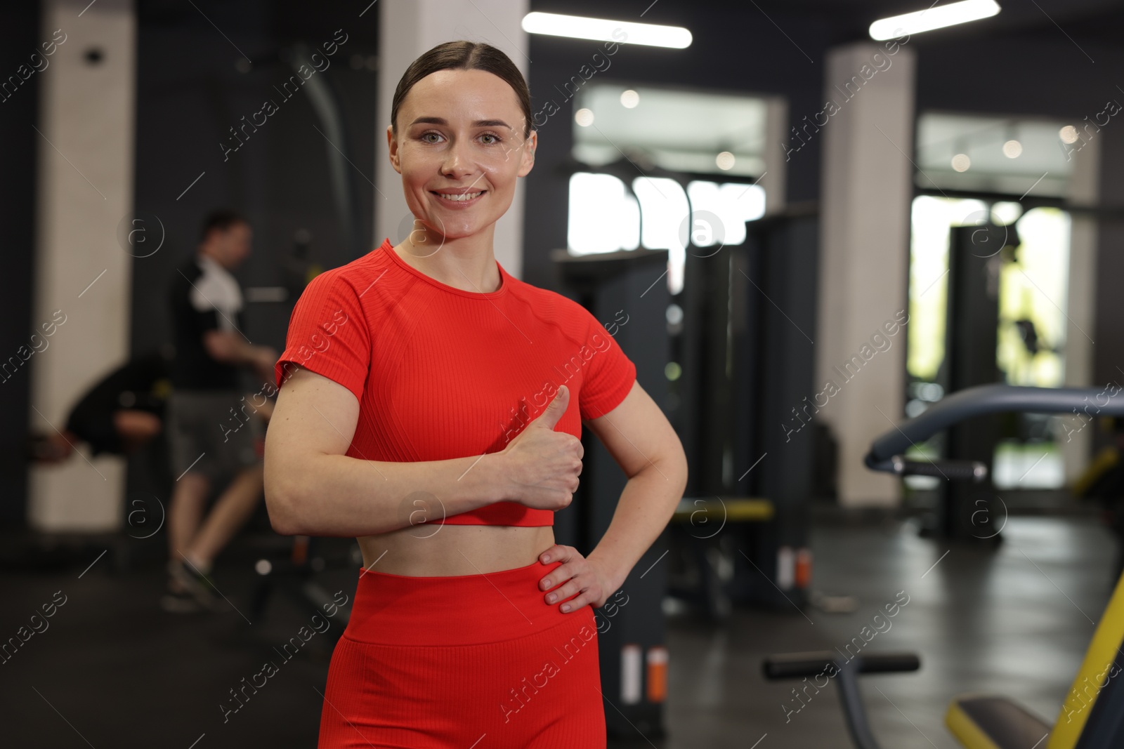 Photo of Personal trainer showing thumbs up in gym. Space for text
