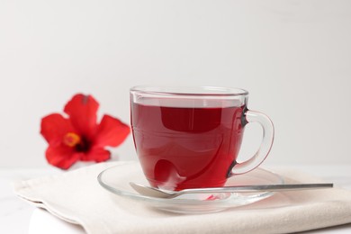 Photo of Delicious hibiscus tea in glass cup and spoon on white table, closeup