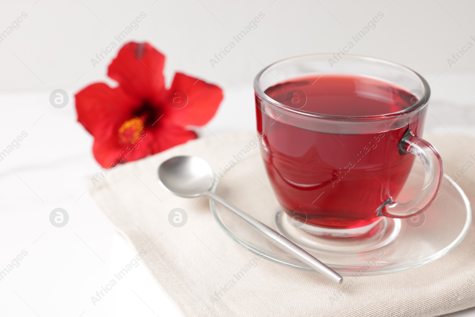 Delicious hibiscus tea in glass cup and spoon on white table, closeup. Space for text Photo of Delicious hibiscus tea in glass cup and spoon on white table, closeup. Space for text