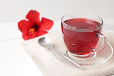 Photo of Delicious hibiscus tea in glass cup and spoon on white table, closeup. Space for text