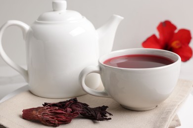 Photo of Delicious hibiscus tea in cup, teapot and dry roselle sepals on white table, closeup