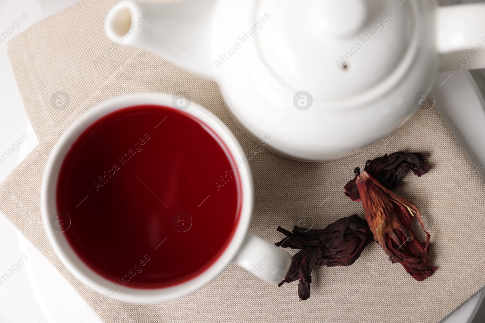 Delicious hibiscus tea in cup, teapot and dry roselle sepals on white table, flat lay Photo of Delicious hibiscus tea in cup, teapot and dry roselle sepals on white table, flat lay
