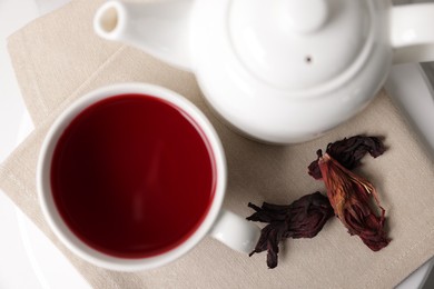 Photo of Delicious hibiscus tea in cup, teapot and dry roselle sepals on white table, flat lay
