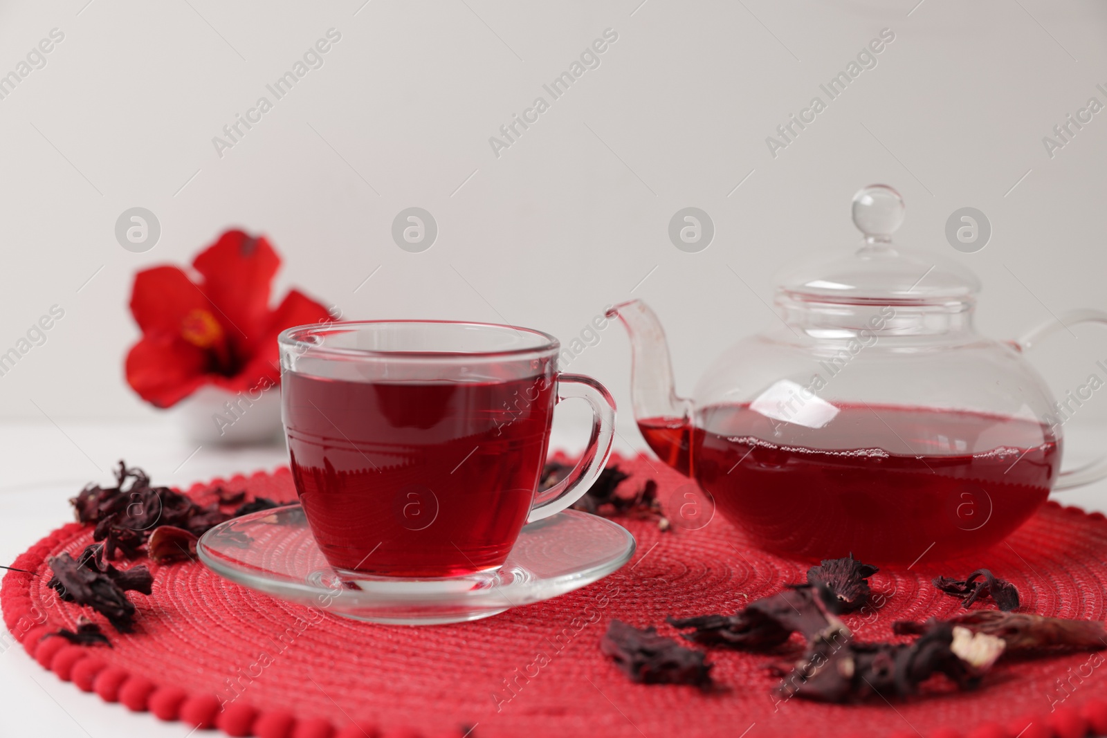 Delicious hibiscus tea in glass cup, teapot and dry roselle sepals on white table, closeup Photo of Delicious hibiscus tea in glass cup, teapot and dry roselle sepals on white table, closeup
