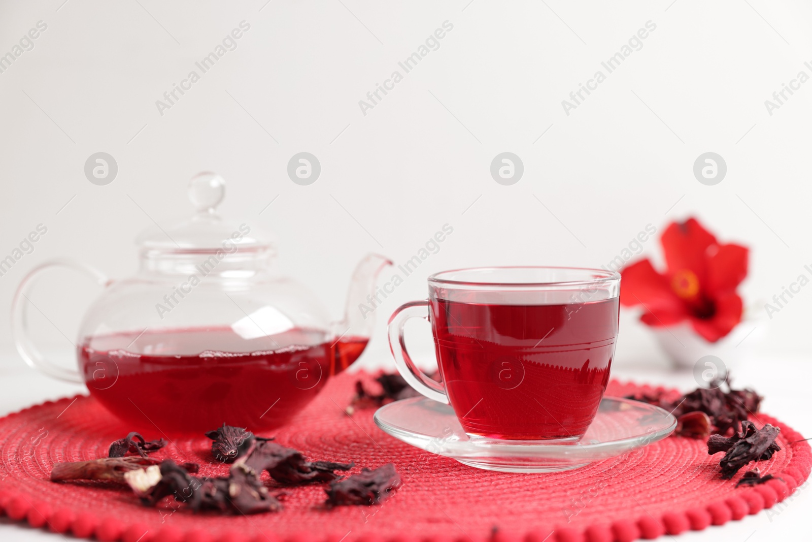 Delicious hibiscus tea in glass cup, teapot and dry roselle sepals on white table, closeup Photo of Delicious hibiscus tea in glass cup, teapot and dry roselle sepals on white table, closeup