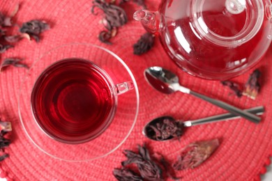Photo of Delicious hibiscus tea in glass cup, teapot, dry roselle sepals and spoons on table, flat lay