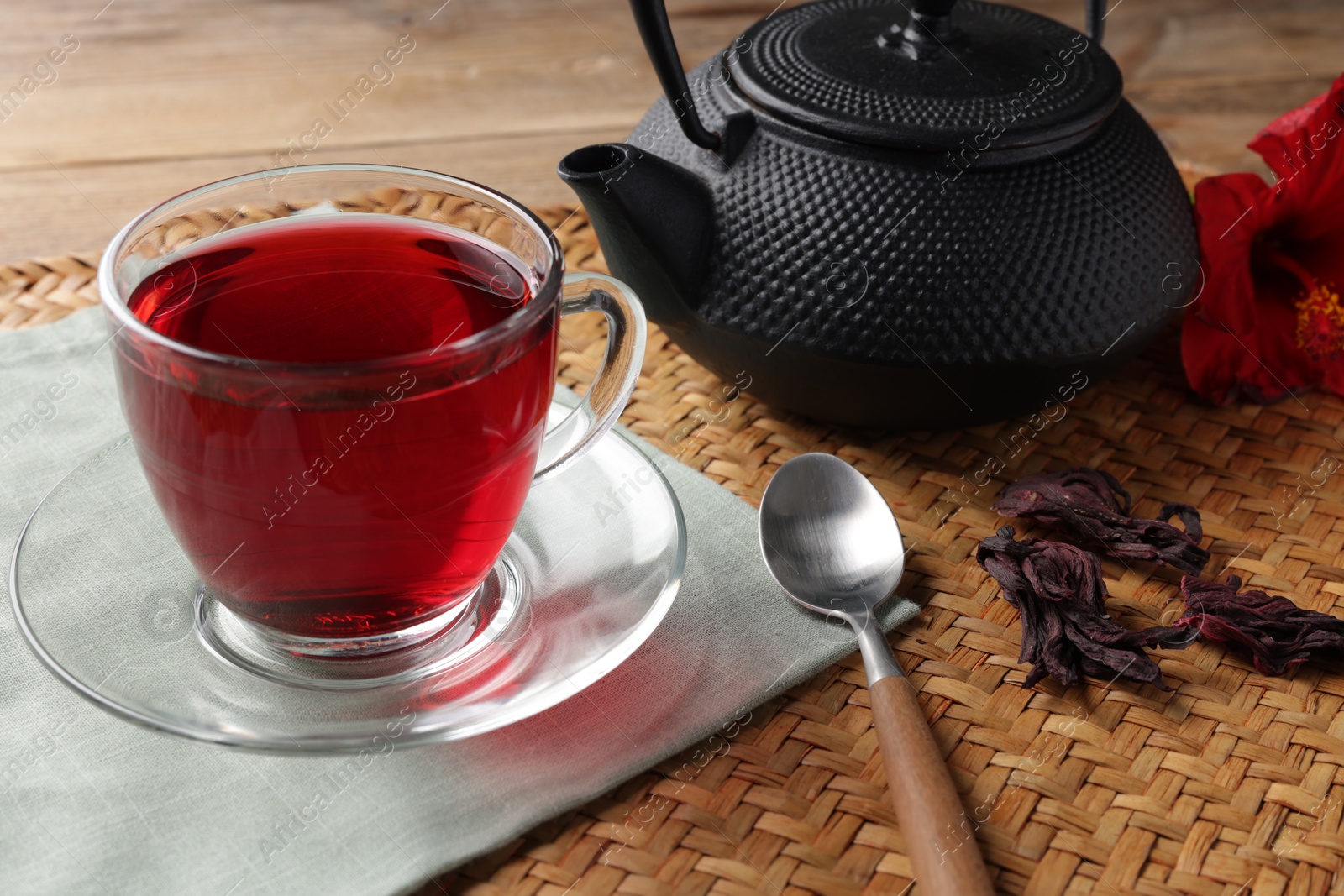 Delicious hibiscus tea in glass cup, teapot, dry roselle sepals and spoon on wooden table, closeup Photo of Delicious hibiscus tea in glass cup, teapot, dry roselle sepals and spoon on wooden table, closeup
