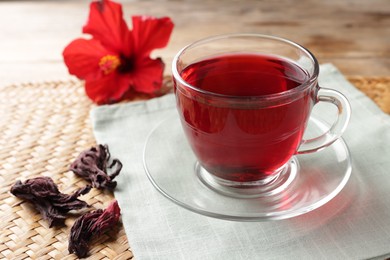 Photo of Delicious hibiscus tea in glass cup and dry roselle sepals on wooden table, closeup