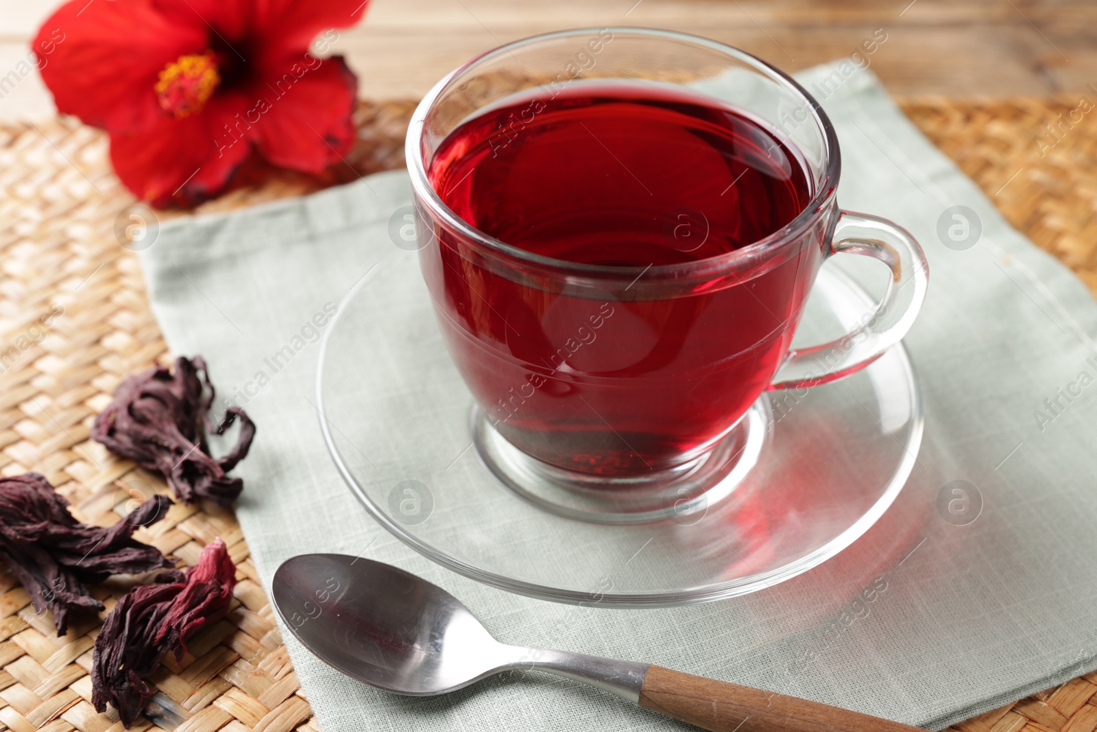 Delicious hibiscus tea in glass cup, dry roselle sepals and spoon on table, closeup Photo of Delicious hibiscus tea in glass cup, dry roselle sepals and spoon on table, closeup