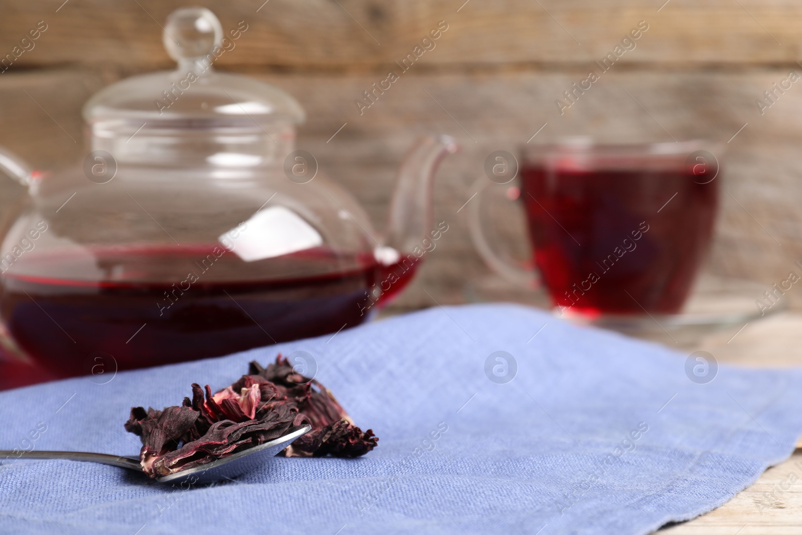 Delicious hibiscus tea in glass cup, teapot, dry roselle sepals and spoon on wooden table, closeup. Space for text Photo of Delicious hibiscus tea in glass cup, teapot, dry roselle sepals and spoon on wooden table, closeup. Space for text