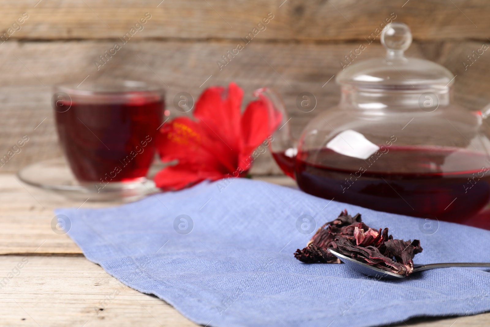 Delicious hibiscus tea in glass cup, teapot, dry roselle sepals and spoon on wooden table, closeup. Space for text Photo of Delicious hibiscus tea in glass cup, teapot, dry roselle sepals and spoon on wooden table, closeup. Space for text