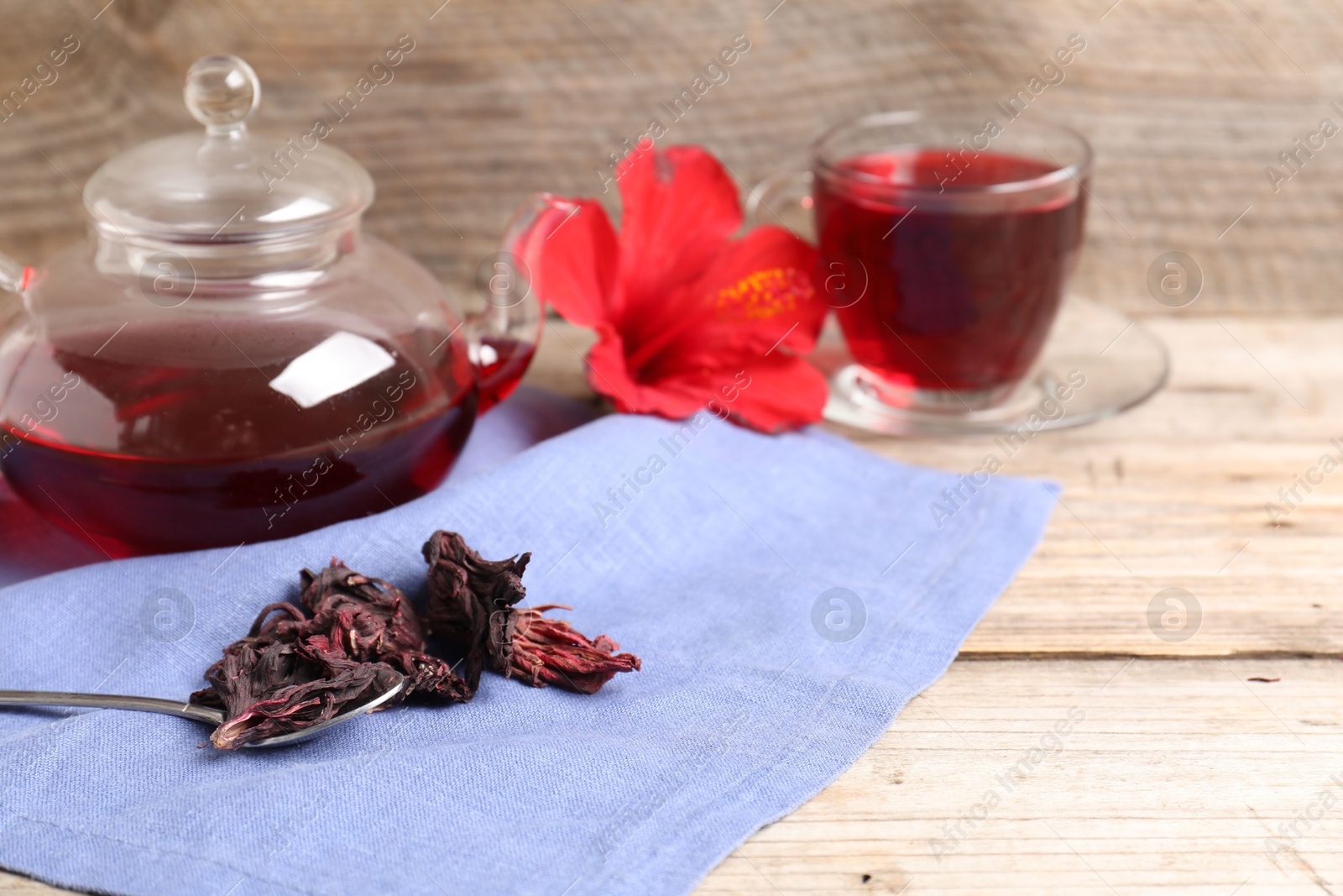 Delicious hibiscus tea in glass cup, teapot, dry roselle sepals and spoon on wooden table, closeup. Space for text Photo of Delicious hibiscus tea in glass cup, teapot, dry roselle sepals and spoon on wooden table, closeup. Space for text