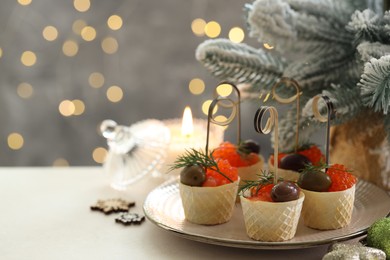 Photo of Tasty canapes and festive decor on white table against blurred lights, closeup. Space for text